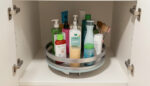 A lazy Susan turntable loaded with bathroom products, positioned inside a deep under-sink cabinet for easy access.