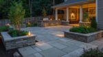 Natural paving stone patio at ground level with built-in garden beds, outdoor kitchen and ambient lighting