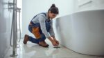 Plumber installing floor-mounted tapware and waste fitting for freestanding bathtub during bathroom renovation